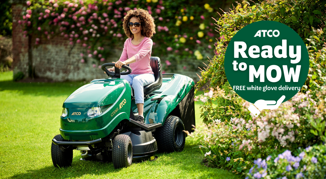 Lady riding ATCO ride-on mower in garden with 'ready to mow' logo banner