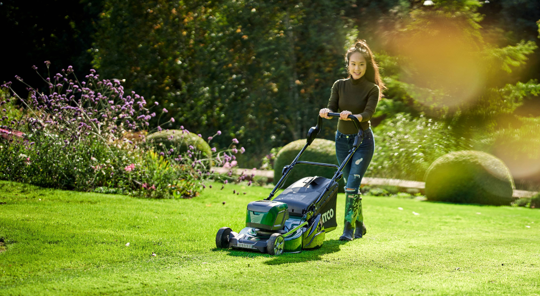 Woman mowing lawn with an ATCO Battery Liner roller mower in spring garden