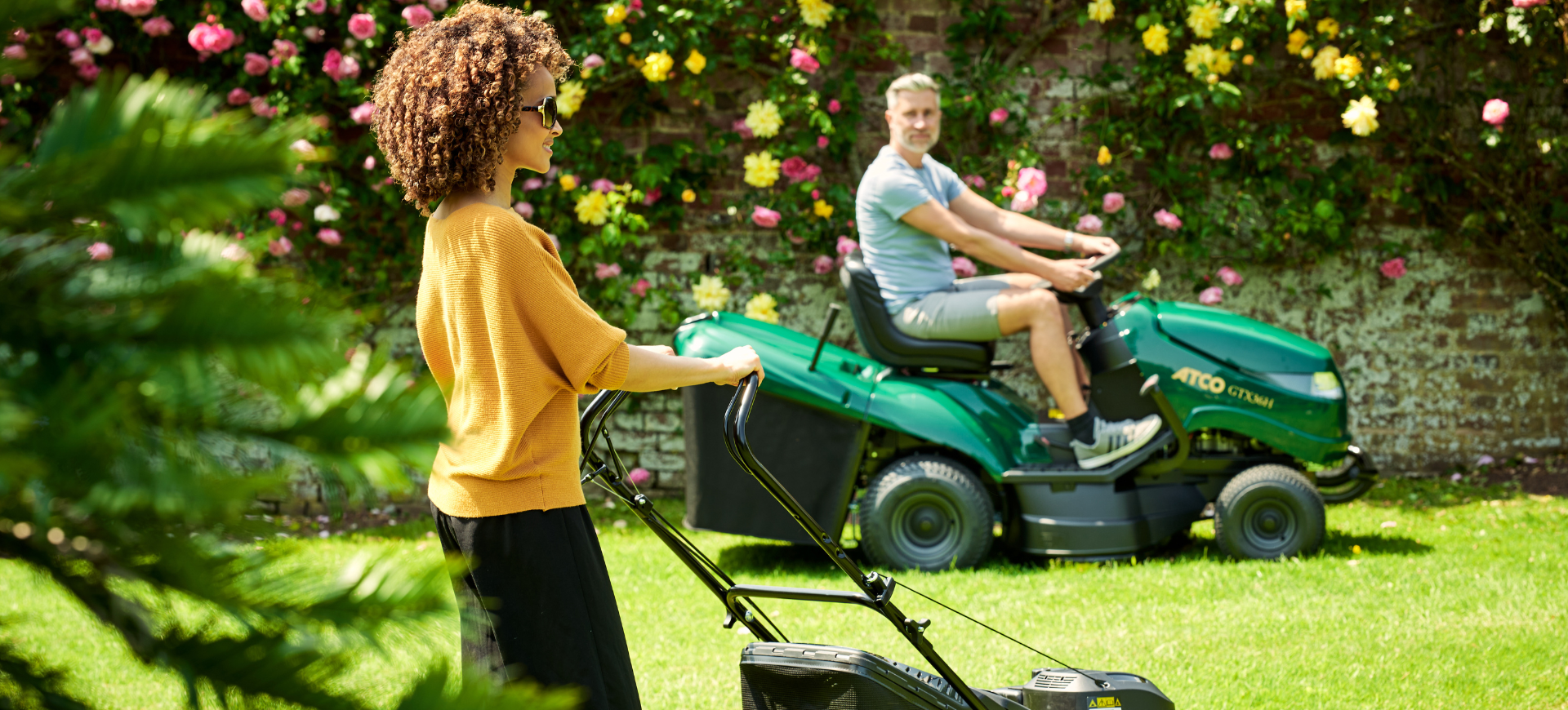 Man on ATCO ride-on mower and woman with walkbehind mower mowing garden